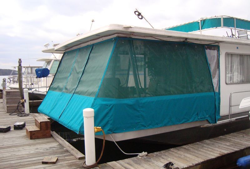 A houseboat with teal and green canvas side covers is docked.