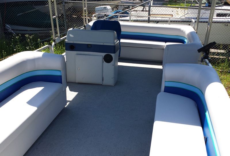 Pontoon boat interior with white, blue, and gray seating and dashboard; outdoors.