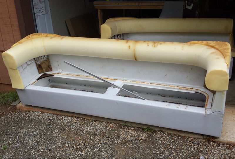 A gray sofa frame with exposed foam padding. A metal bar is inside. Outdoors, in a yard.