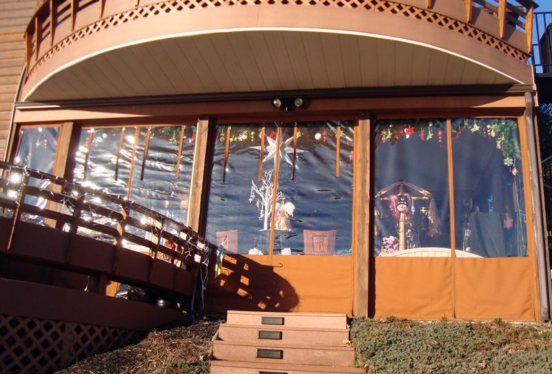 Brown outdoor deck with transparent vinyl curtains, steps, and railing.
