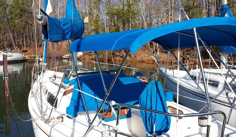 Blue-canopied sailboat docked at a marina with trees in the background.