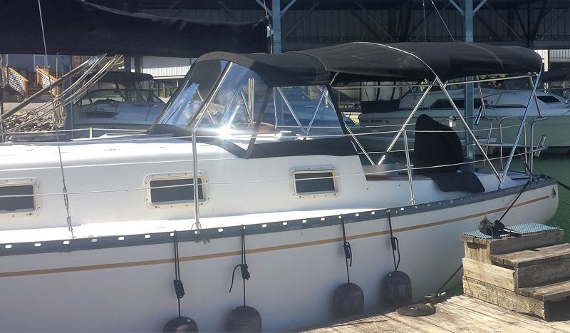 Sailboat docked at a marina with a black canopy and clear window panels.