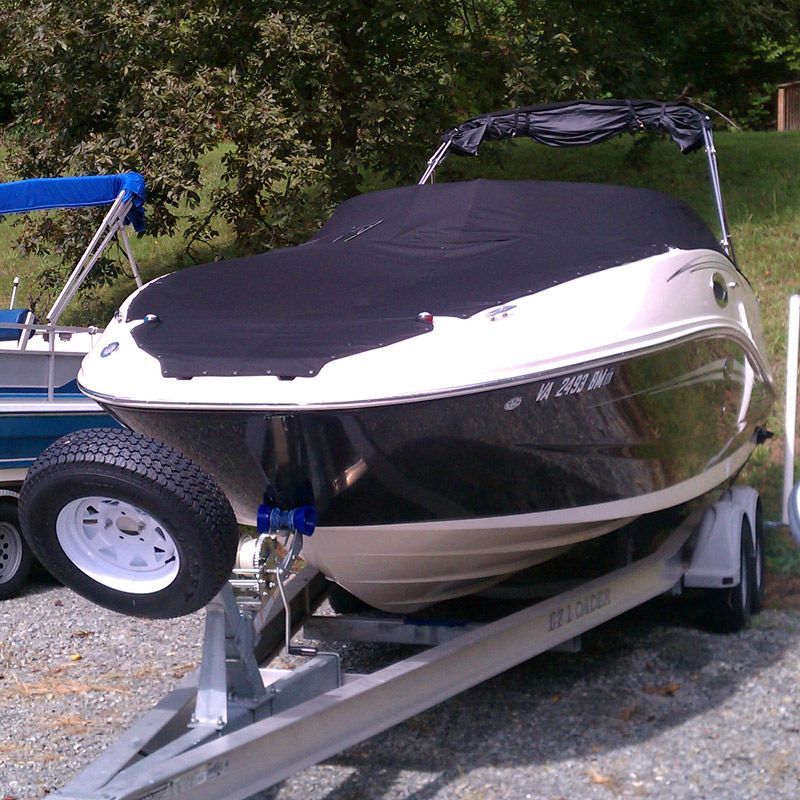 Boat covered in black, on a trailer. White and black boat with a spare tire.