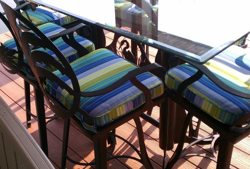Outdoor bar stools with striped cushions around a glass table on a wooden deck.