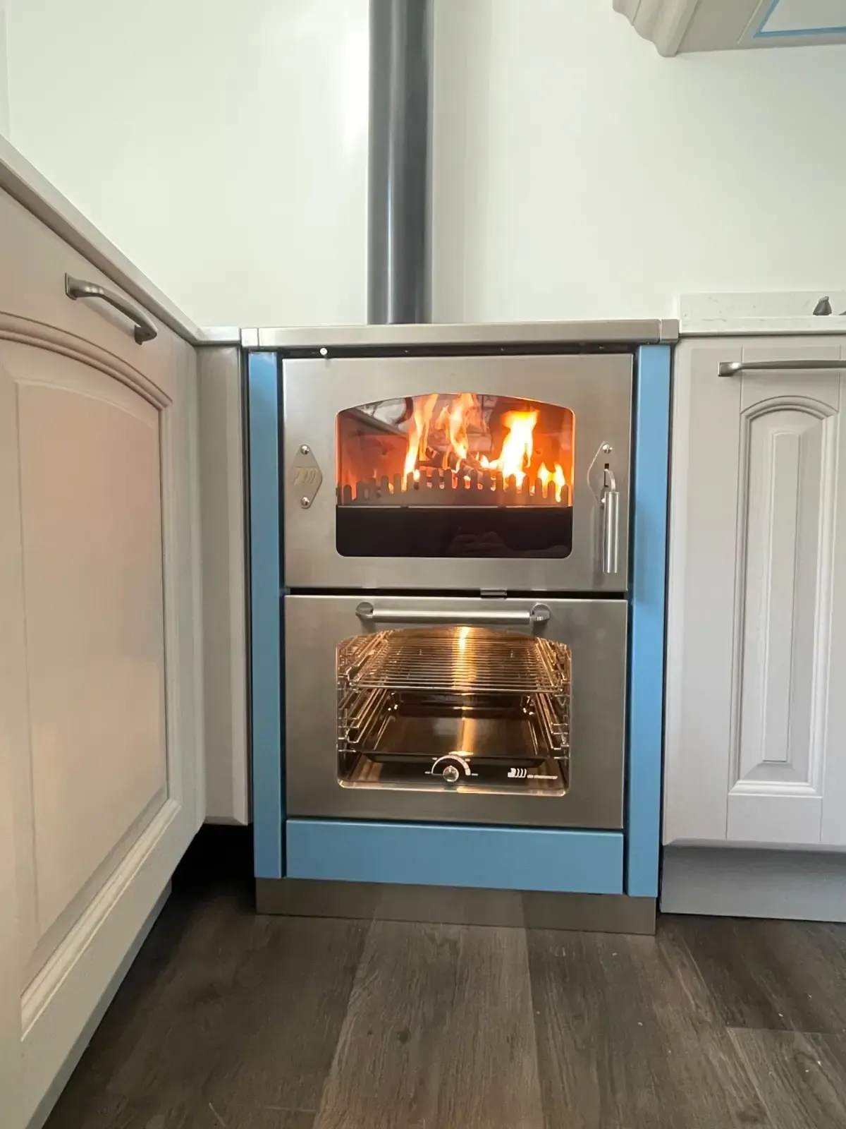Una stufa a legna con fuoco acceso, dettagli in acciaio inossidabile e un camino nero in una cucina moderna.
