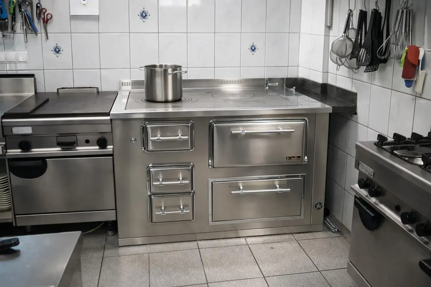Cucina commerciale in acciaio inox con fornelli e forni. Una pentola è appoggiata sul piano cottura.