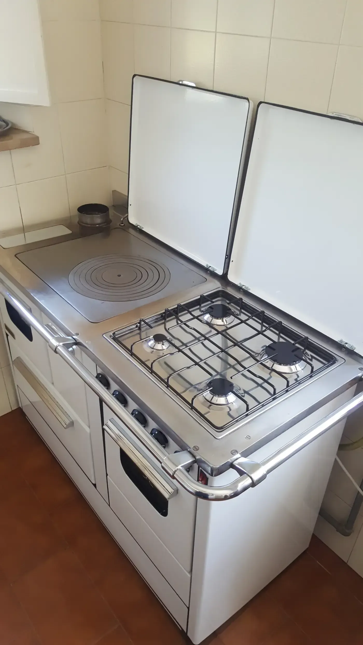 Cucina a gas bianca e argento con piano cottura, bruciatori e coperchi rialzati.