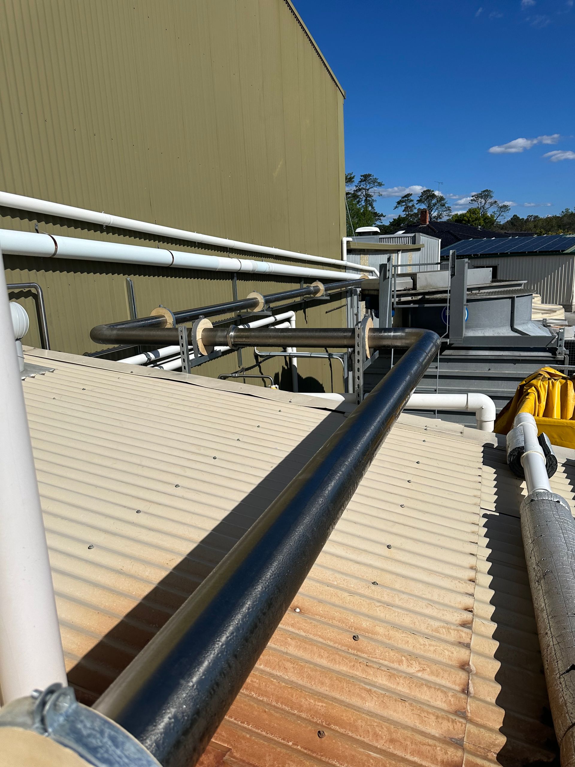 Industrial rooftop with black pipes and beige building walls under a blue sky — EB Metalworks in Somersby, NSW