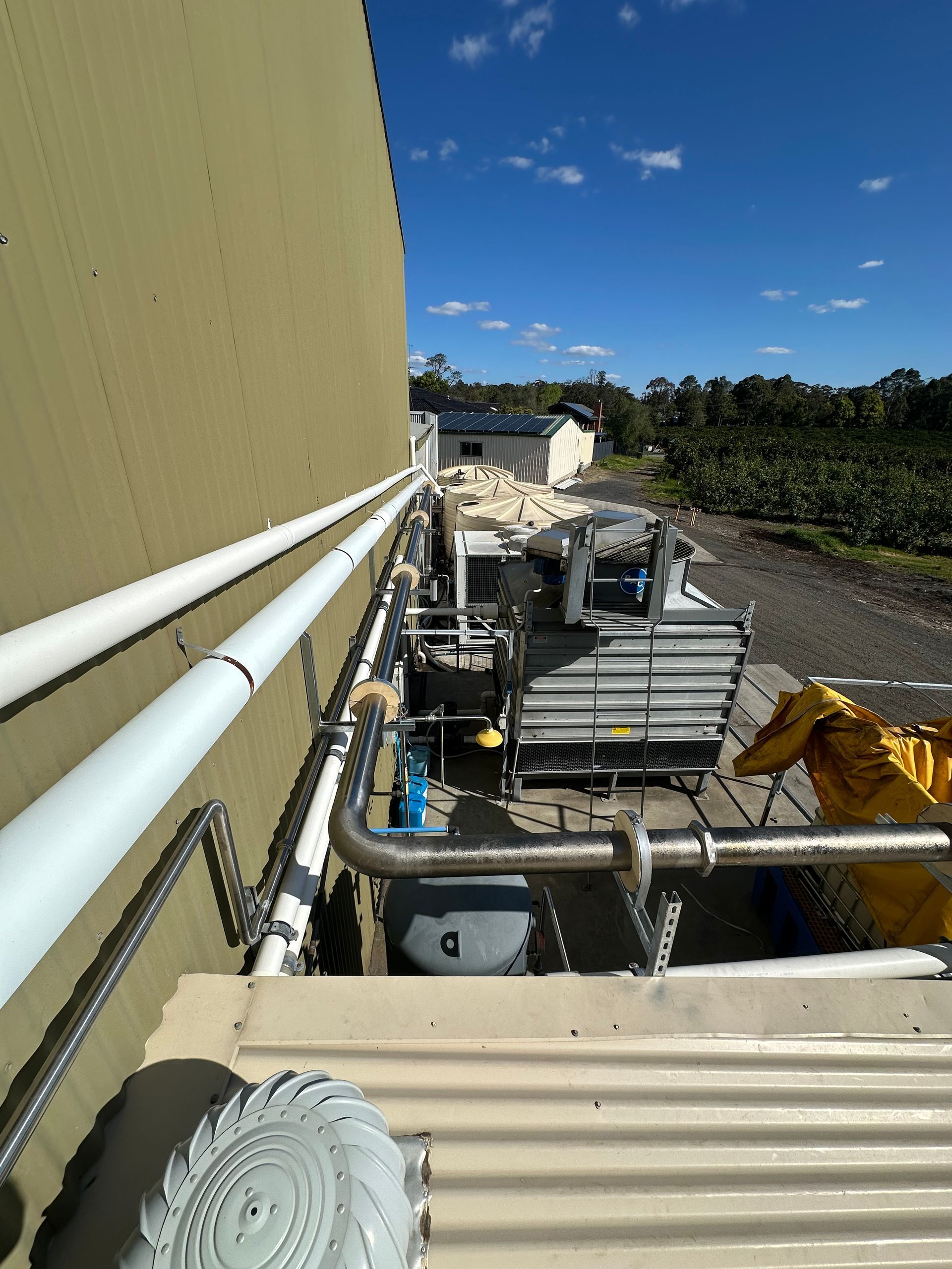 Industrial machinery beside a building wall under a clear blue sky, with pipes and equipment in the foreground — EB Metalworks in Somersby, NSW