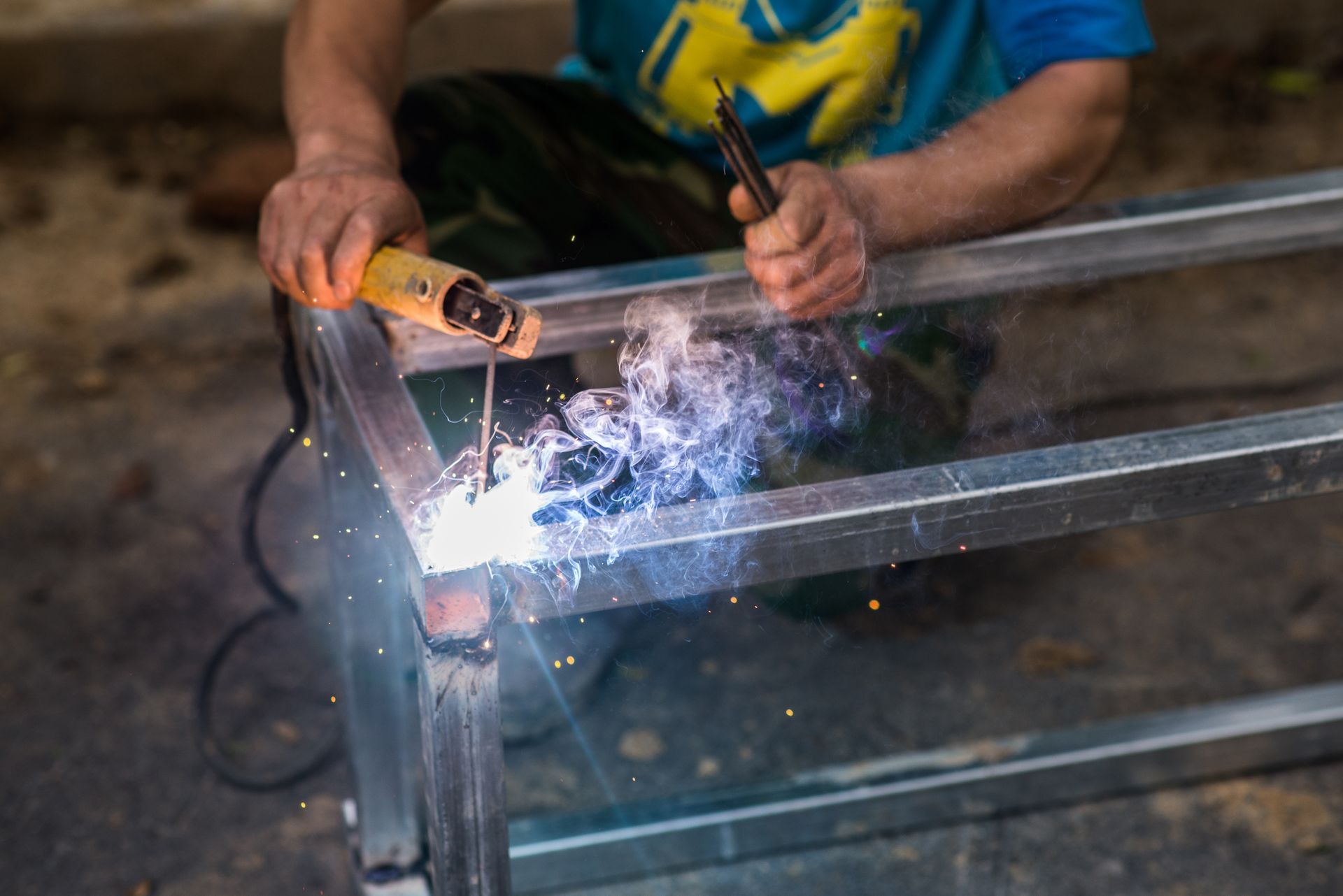 Welder Using a Welding Torch to Join Metal Bars, Creating Sparks and Smoke in an Indoor Setting — EB Metalworks in Somersby, NSW