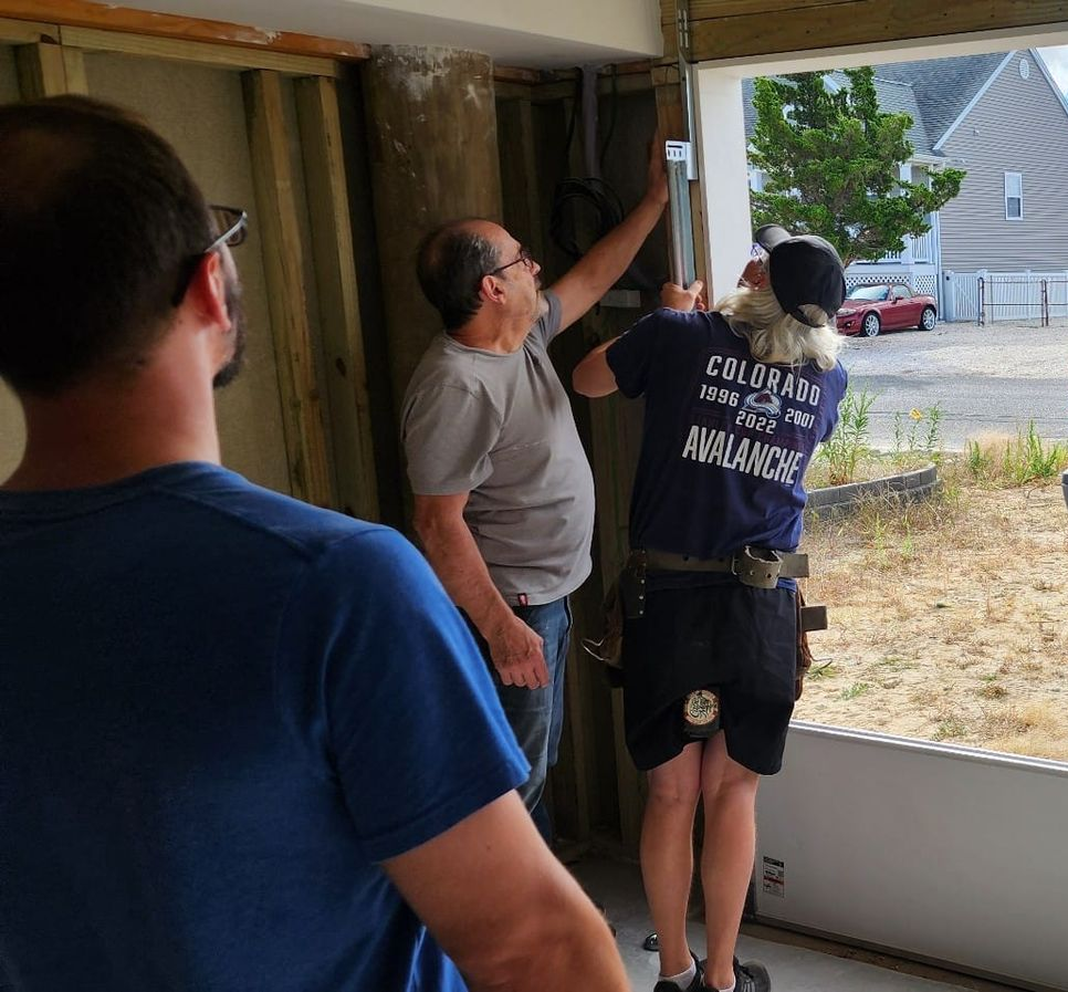 Two people install a metal frame in an open doorway while a third person watches in a room under construction.