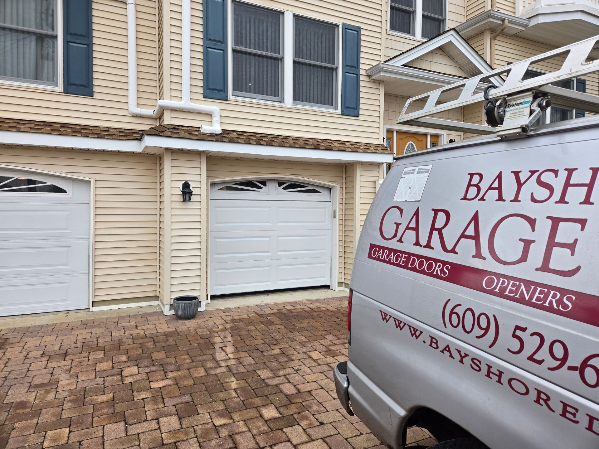 A service van parked in front of a house with two white garage doors and light-colored siding.