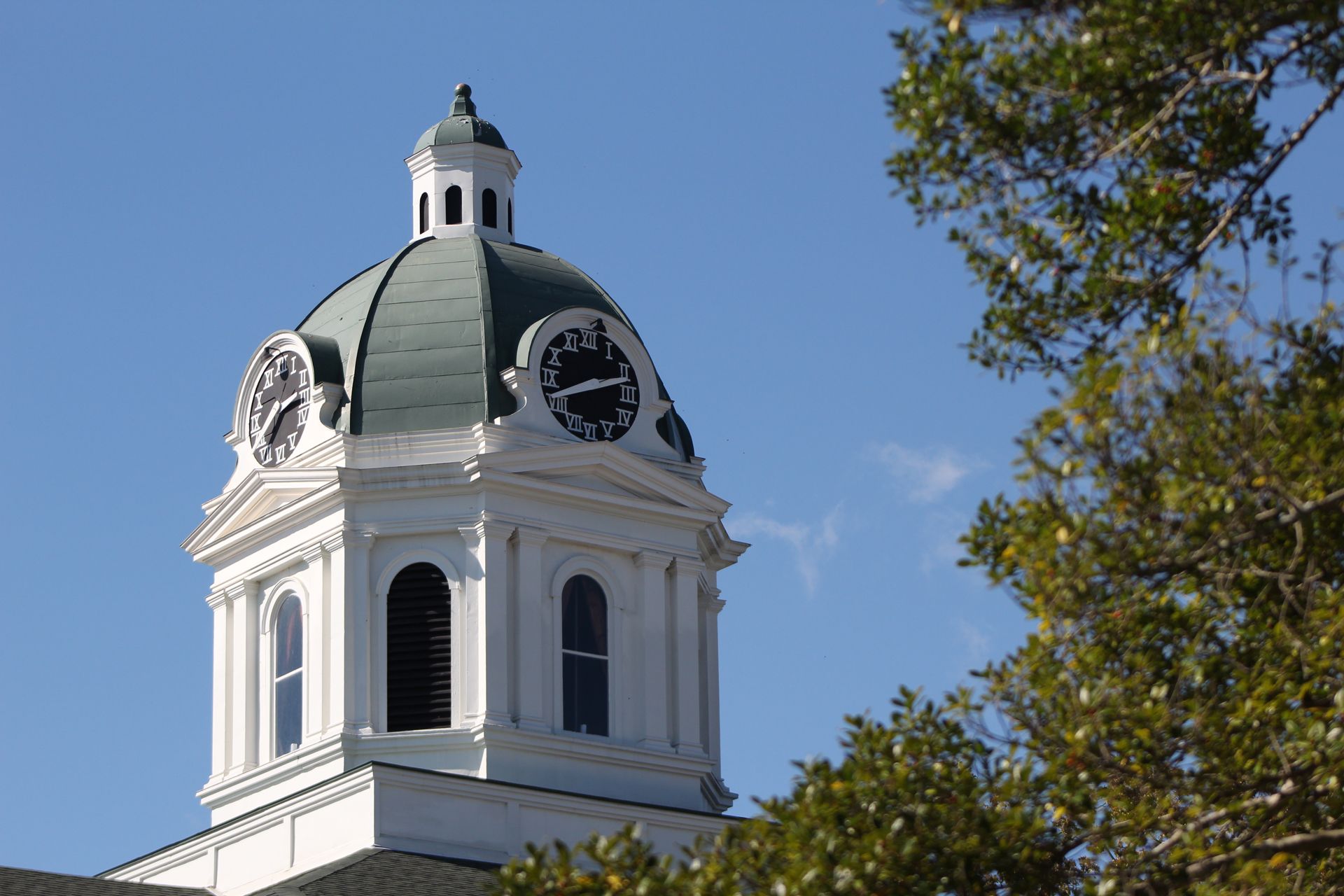 White courthouse dome with clock faces, green roof, and blue sky
