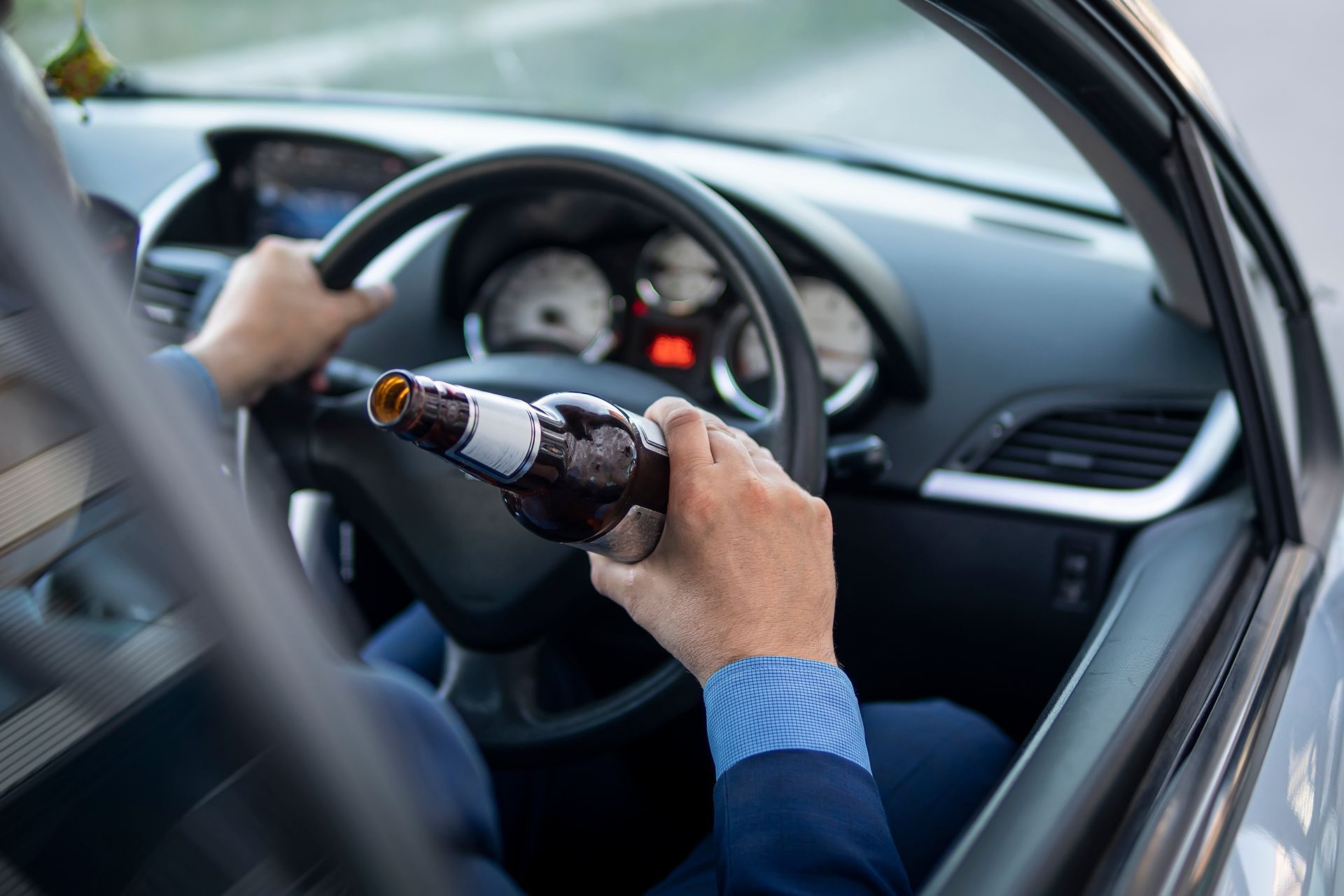 Person in a car holding a beer bottle while driving