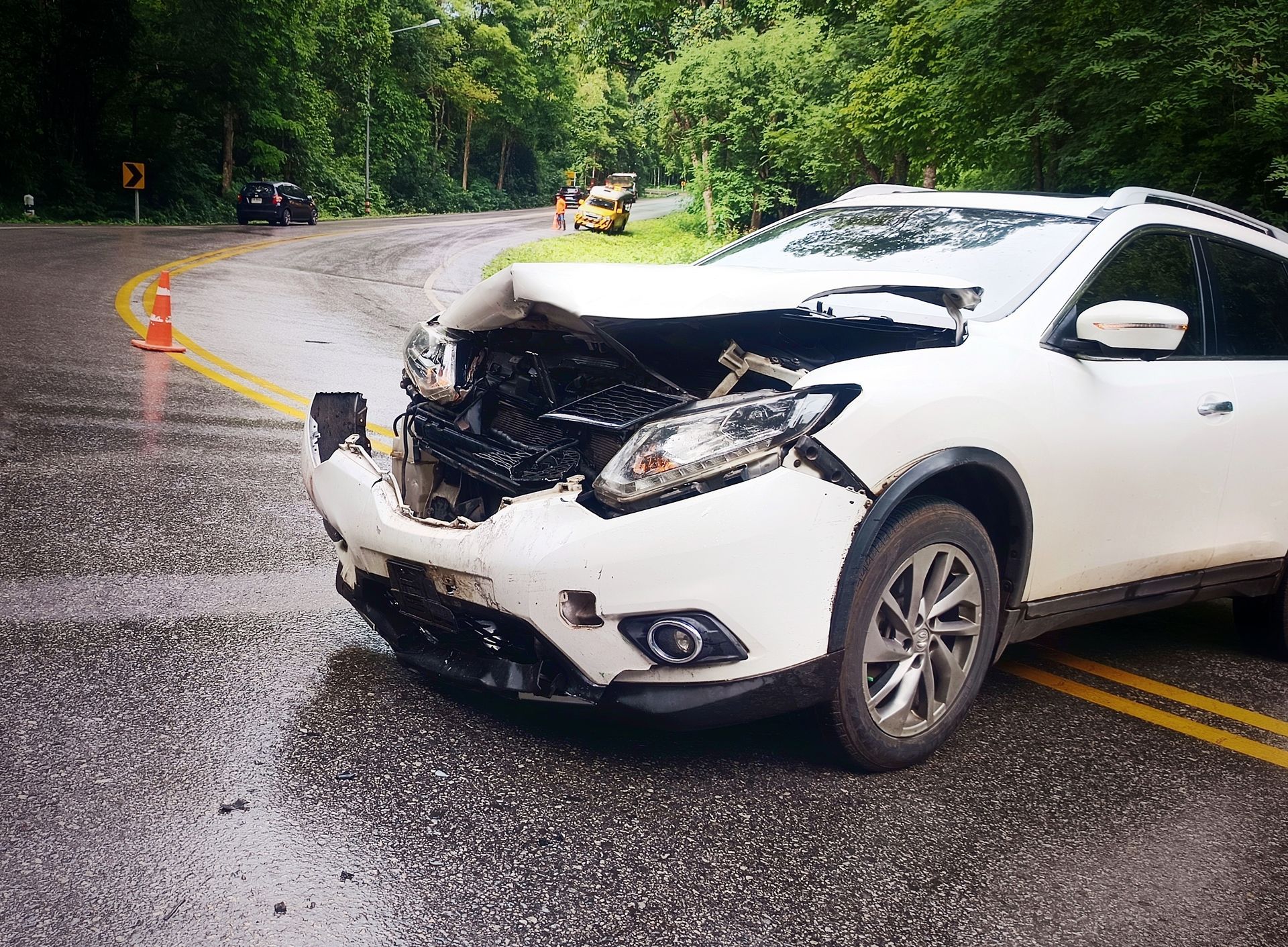 White SUV damaged in a car accident on a wet, curved road in a wooded area