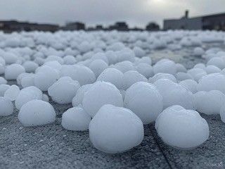 Hailstones cover a flat surface, with a blurred cityscape in the background.