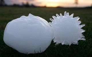 Two large hailstones on grass, one smooth, one with spiky protrusions, under a sunset sky.