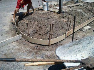 A person is standing in the dirt next to a wheelbarrow and a shovel.