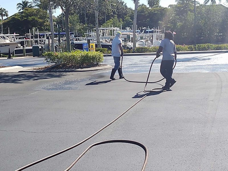 Two men are spraying asphalt in a parking lot