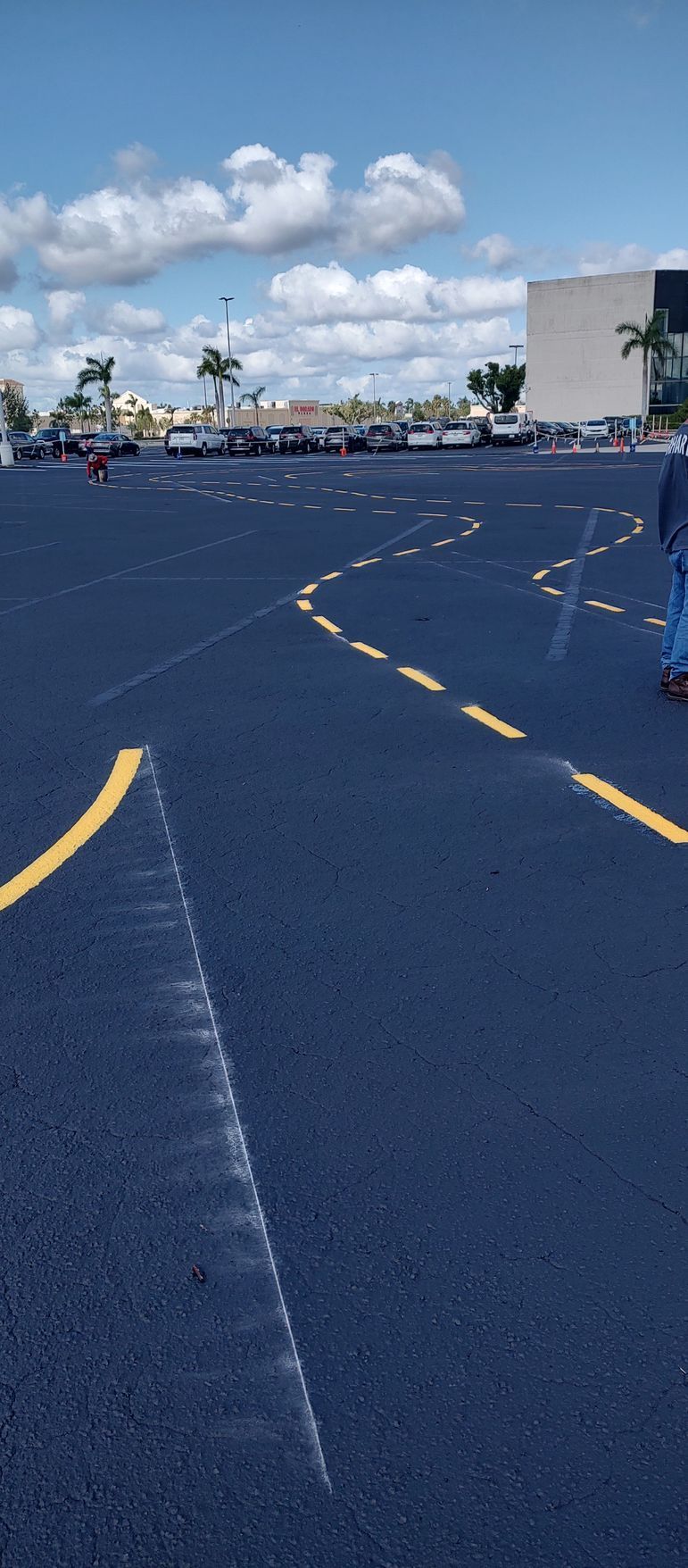 A person is walking down a parking lot with a building in the background.