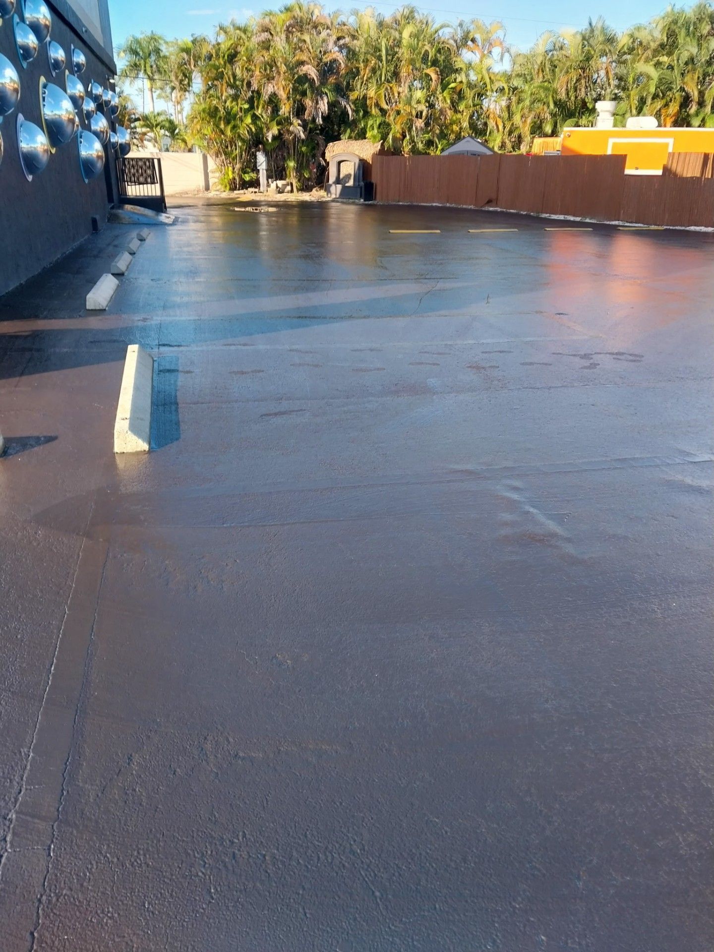 An empty asphalt parking lot, gray and reflective, with white parking bumpers.