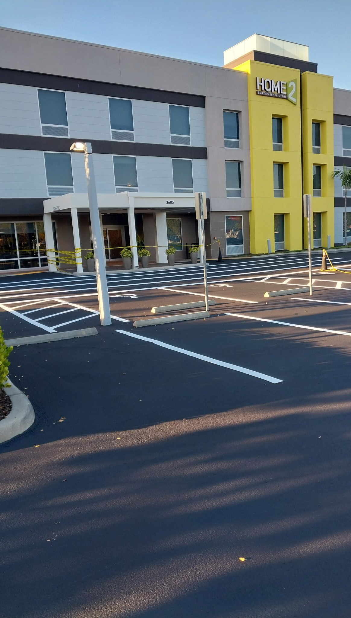 Hotel exterior with grey and yellow sections, parking lot in front, and a blue sky.