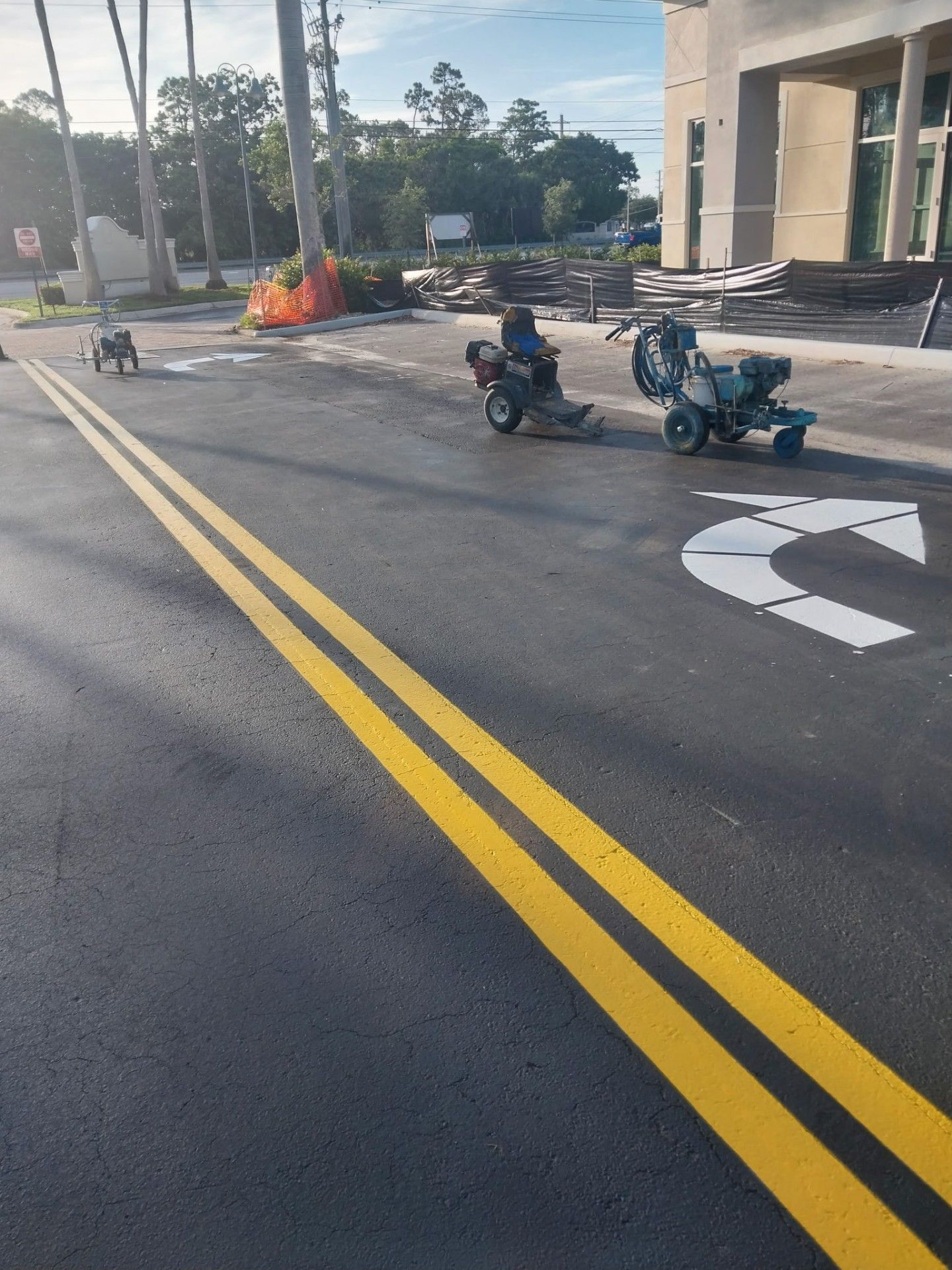 Double yellow lines and turn arrow on fresh asphalt. Road work in progress with three machines.