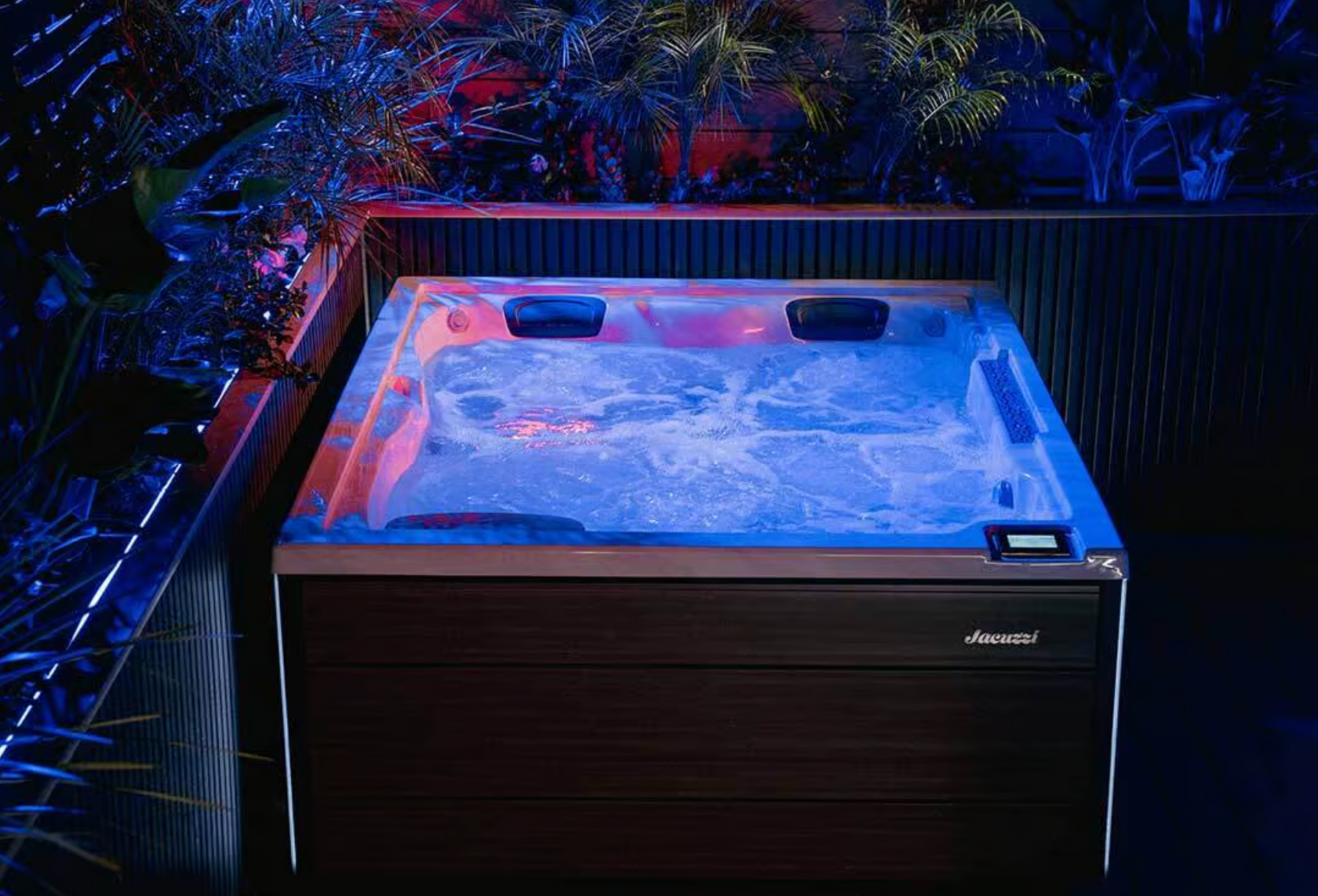 Jacuzzi avec lumières bleues, eau bouillonnante et lambris en bois foncé, entouré de verdure.