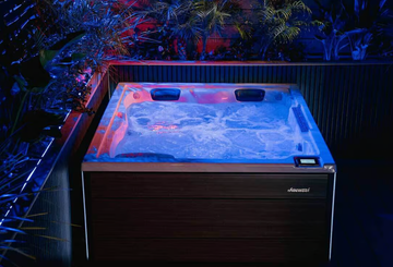 Jacuzzi avec lumières bleues, eau bouillonnante et lambris en bois foncé, entouré de verdure.