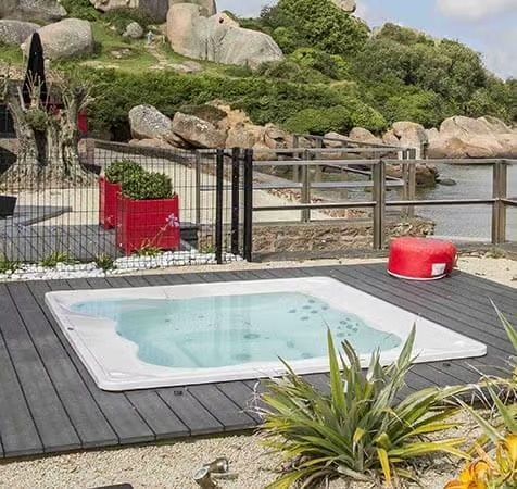 Un patio avec une table et des chaises et un parasol avec un bain à remous en arrière-plan.