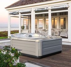 Un bain à remous est installé sur une terrasse en bois devant une maison.