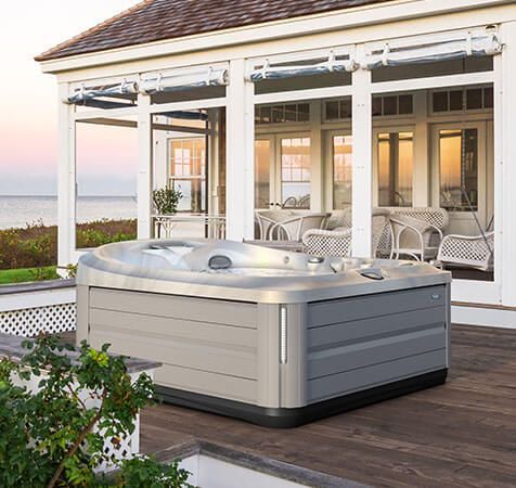 Un bain à remous est installé sur une terrasse en bois devant une maison.