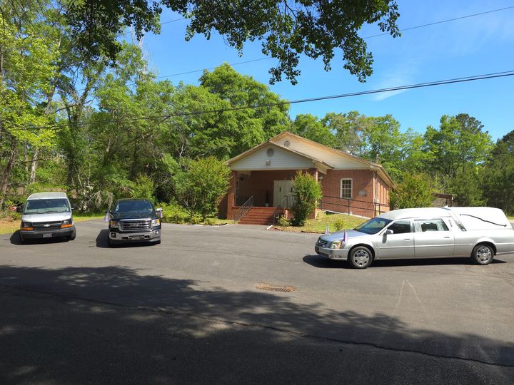 Silver hearse parked in front of a brick church on a sunny day.