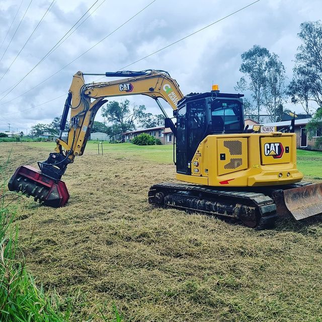 A Yellow Cat Excavator Is Cutting Grass in A Field — CK's Milling & Earthworks in Bells Bridge, QLD