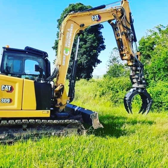 A Yellow Cat Excavator Is Parked in A Grassy Field — CK's Milling & Earthworks in Gympie, QLD