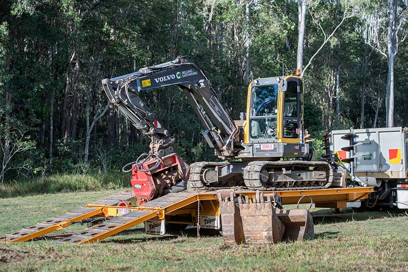 A Large Excavator Is Sitting on Top of A Ramp in A Field — CK's Milling & Earthworks in Bells Bridge, QLD