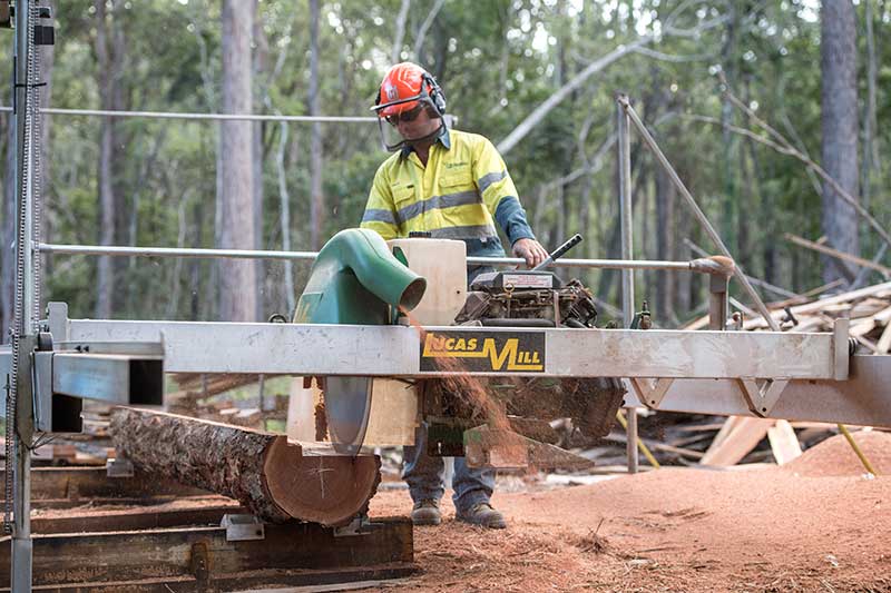 A Man Is Cutting a Log with A Machine in The Woods — CK's Milling & Earthworks in Bells Bridge, QLD