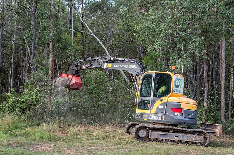 A Yellow and Black Excavator Is Cutting Trees in A Forest — CK's Milling & Earthworks in Bells Bridge, QLD