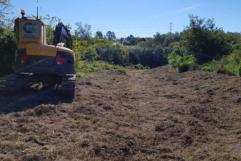 A Yellow Excavator Is Driving Through a Dirt Field — CK's Milling & Earthworks in Bells Bridge, QLD
