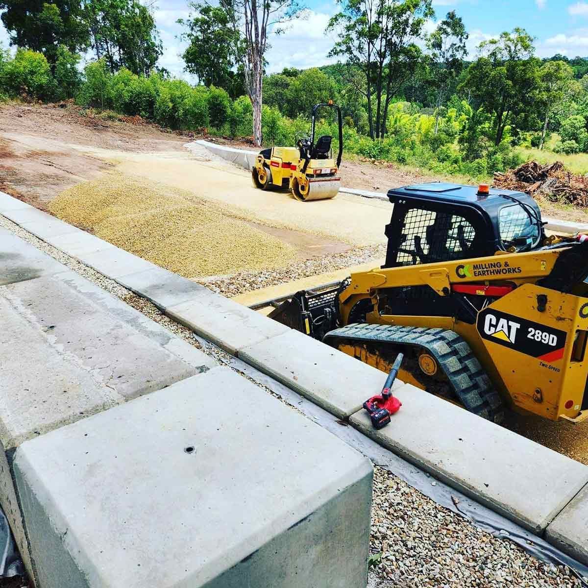 A Yellow Cat Tractor Is Driving Down a Dirt Road — CK's Milling & Earthworks in Bauple, QLD