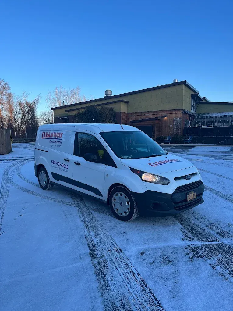 A white van is parked in the snow in front of a building.