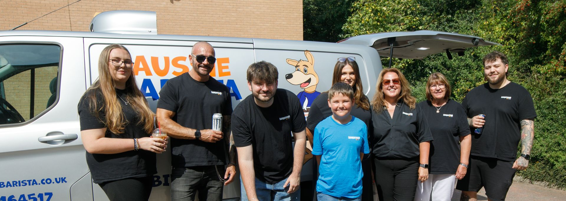 Group of people in black shirts standing near a white van with a dog logo, smiling for a photo.