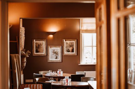 Restaurant interior with framed artwork, tables, and a window, warm colors.