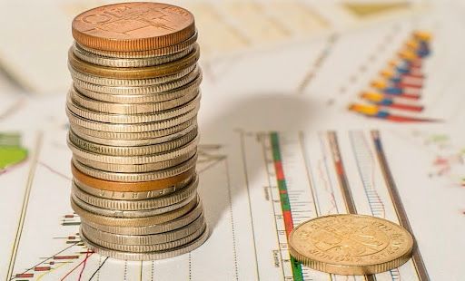 Stack of coins on top of a financial chart, with a loose coin on the bottom right.