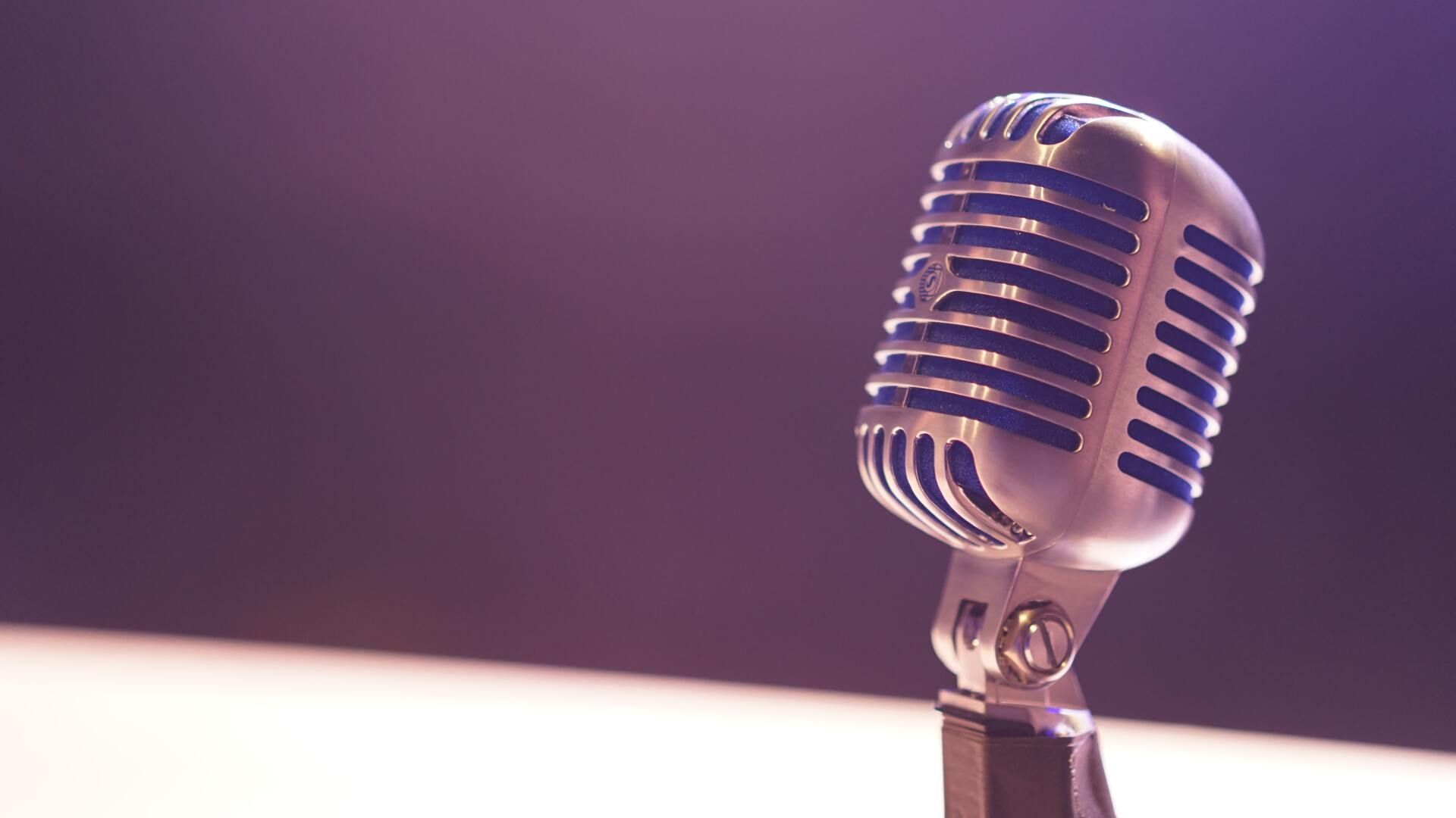 Vintage silver microphone on a stand, lit with purple and white light.