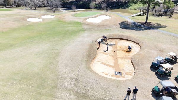 An aerial view of a golf course with golf carts and people playing golf.