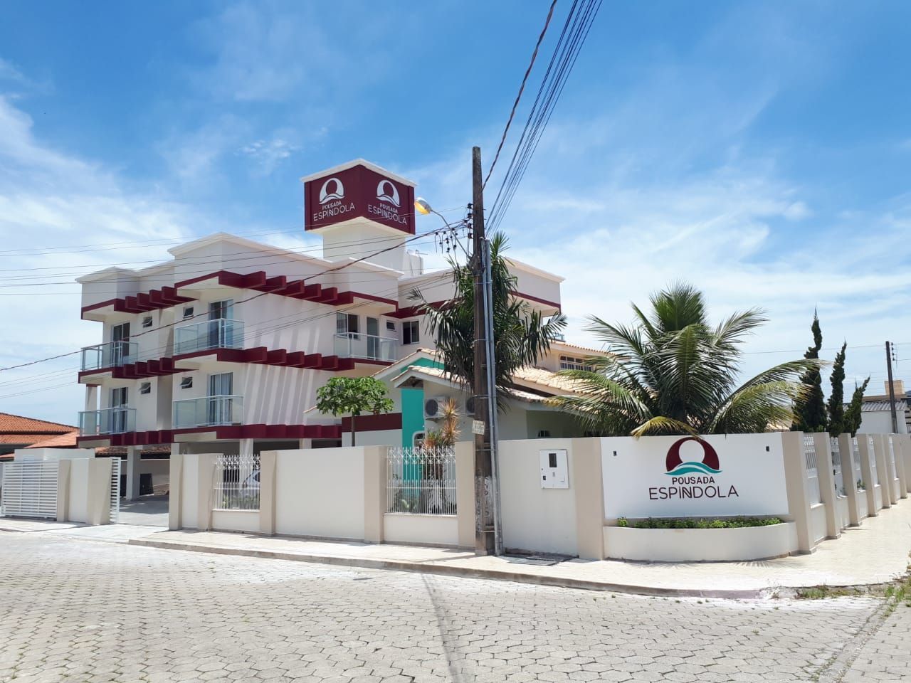 Um hotel com prédio branco e vermelho, com o nome "Espírita" em uma placa. Fica em uma esquina, sob um céu azul.