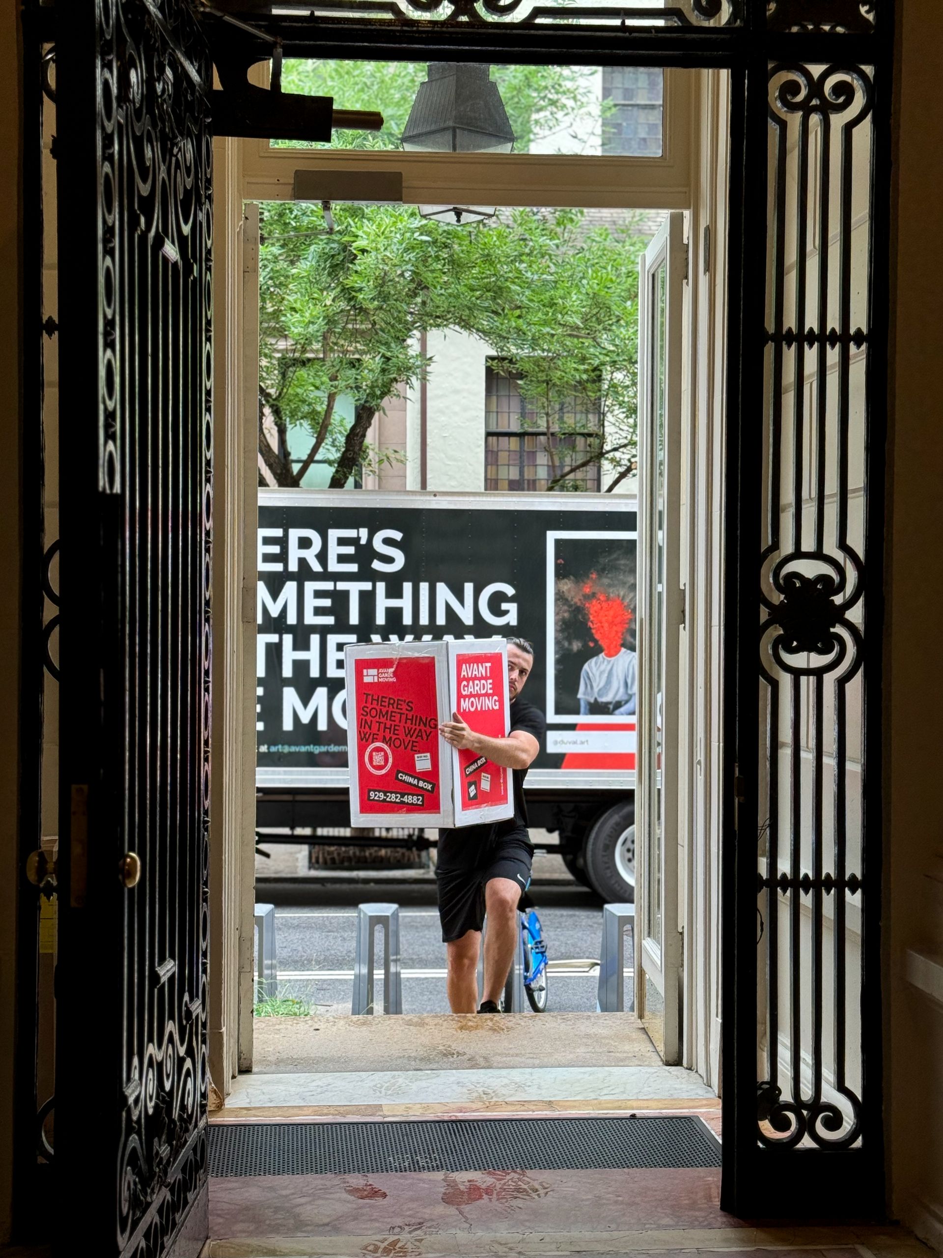 Avant-Garde mover is carrying a box in front of a truck into the apartment building in Upper East Side, Manhattan