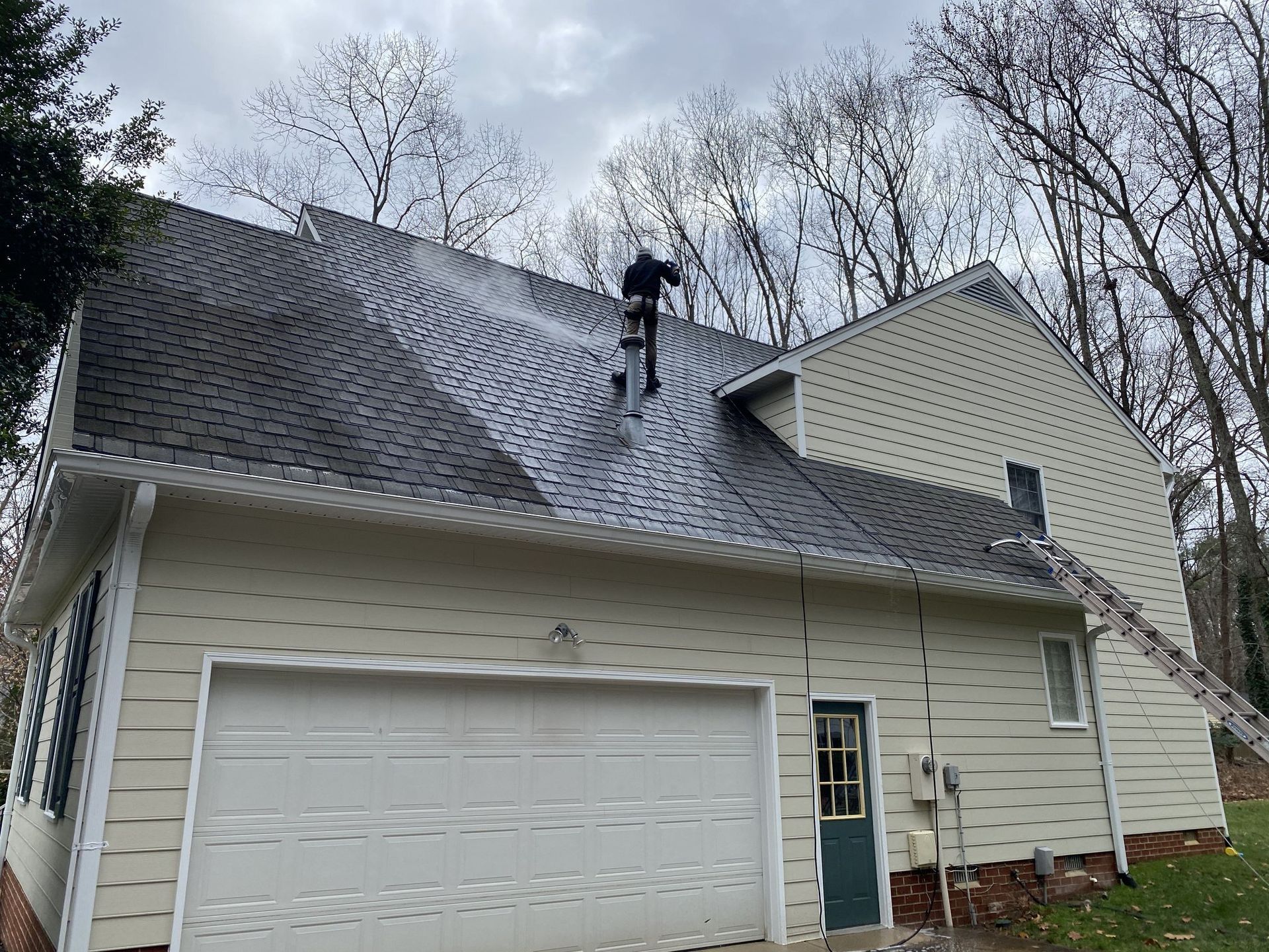 A man is cleaning the roof of a house with a pressure washer.