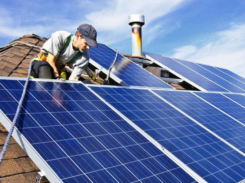 Vyras ant namo stogo montuoja saulės baterijas